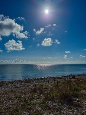 Bu nefes kesici kıyı manzarası büyüleyici suyu, sıcak güneş ışığını ve dağınık bulutları güzel bir şekilde sergiliyor.