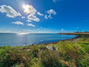Berrak mavi gökyüzünün altında canlı yeşillik ve ışıl ışıl su barındıran nefes kesici bir manzara.