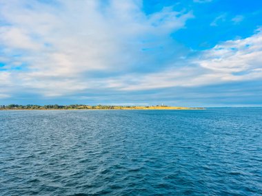 Yeşil kıyı şeridi ve mavi gökyüzü ile huzurlu bir okyanus manzarası, rahatlama ve gençleşme için mükemmel.