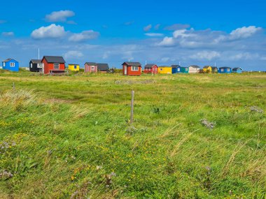 Büyüleyici bir manzara. Renkli kulübeler, yemyeşil bir manzara ve parlak mavi bir gökyüzü üzerine kurulmuş.