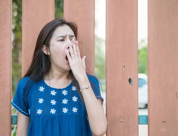 Sleepy asian woman with yawn motion on blurred wooden fence background