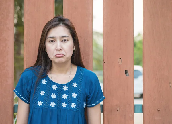 Asian woman with sad face emotion on blurred wooden fence background