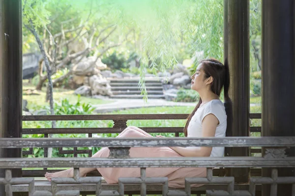 Asyalı kadın dinlenmek için kamu parkta ahşap sandalyede oturan