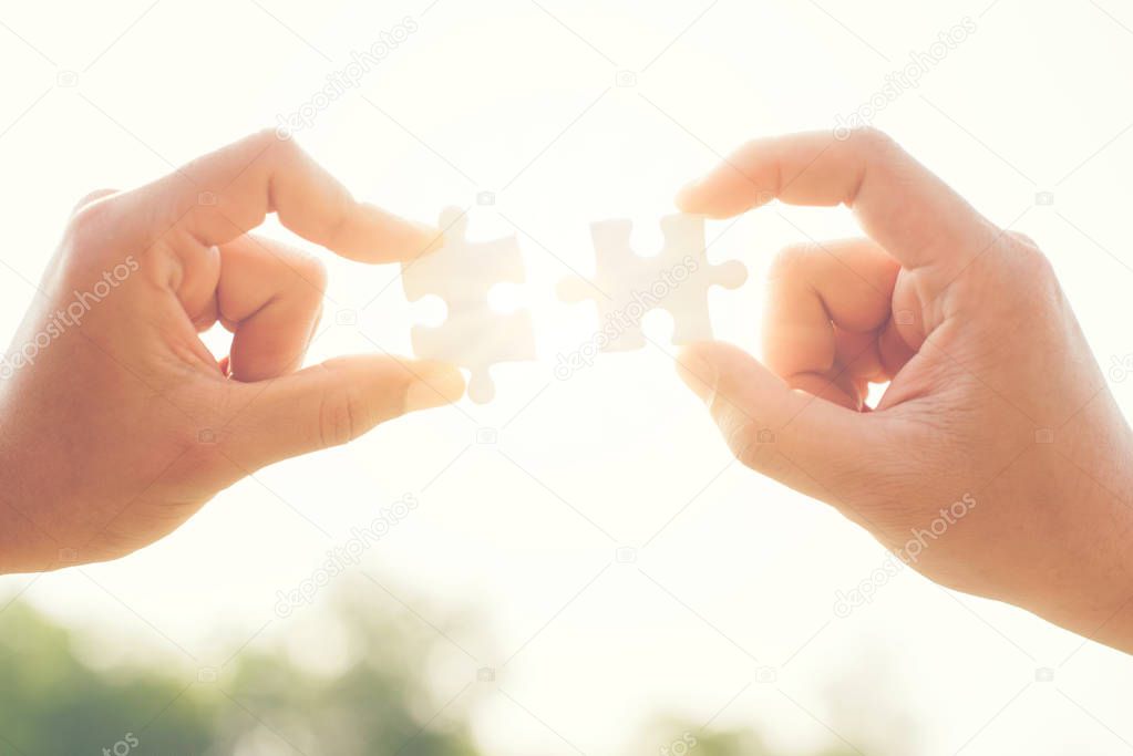 two hands trying to connect couple puzzle piece with sunset background on white.