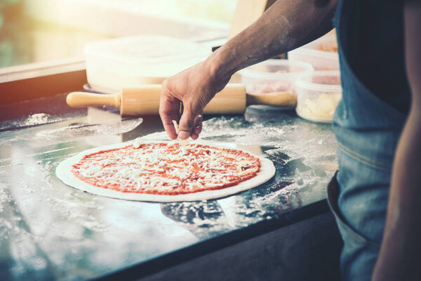 Hand Chef preparing spread cheese on pizza on marble table, closeup making pizza
