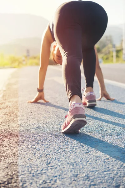 Athlete woman in running start pose on street road. Sport tight clothes. Bright sunset nature mountain blurry background.