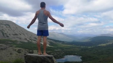 Adam bir dağın tepesinde elleri açık duruyor. Dağın tepesinde, kolları açık bir adam..