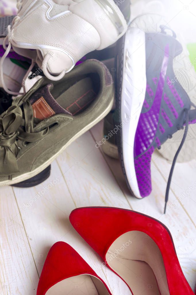 Big heap of different sports shoes and red high heel womens shoes on white background.