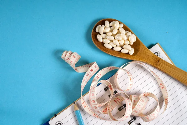 Sheet of Diet Plan and wooden spoon with a measuring tape on a blue background, diet, healthy lifestyle.