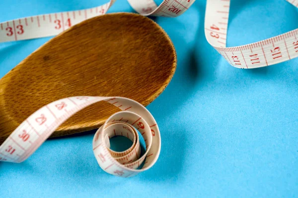 Colher de madeira com uma fita métrica em um fundo azul, dieta, estilo de vida saudável . — Fotografia de Stock