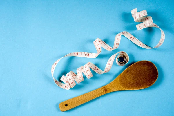 Cuchara de madera con cinta métrica sobre fondo azul, dieta, estilo de vida saludable . — Foto de Stock