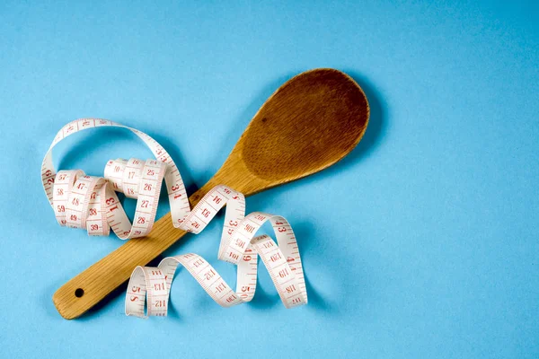 Cuchara de madera con cinta métrica sobre fondo azul, dieta, estilo de vida saludable . — Foto de Stock