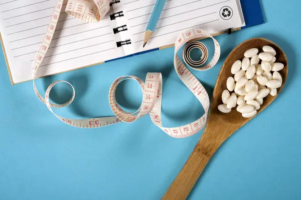 Hoja de plan de dieta y cuchara de madera con una cinta métrica sobre un fondo azul, dieta, estilo de vida saludable . — Foto de Stock