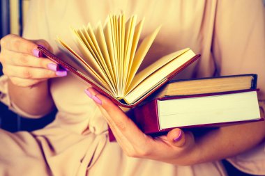 Hafif elbiseli genç kız bir kitap okuyor. Kadın elleri ellerinde bir kitap tutuyor.