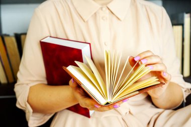 Hafif elbiseli genç kız bir kitap okuyor. Kadın elleri ellerinde bir kitap tutuyor.