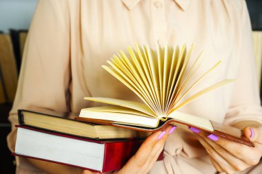 Hafif elbiseli genç kız bir kitap okuyor. Kadın elleri ellerinde bir kitap tutuyor.