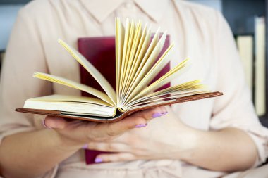 Hafif elbiseli genç kız bir kitap okuyor. Kadın elleri ellerinde bir kitap tutuyor.