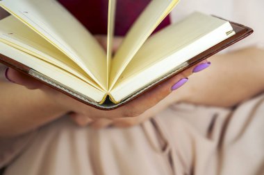 Hafif elbiseli genç kız bir kitap okuyor. Kadın elleri ellerinde bir kitap tutuyor.