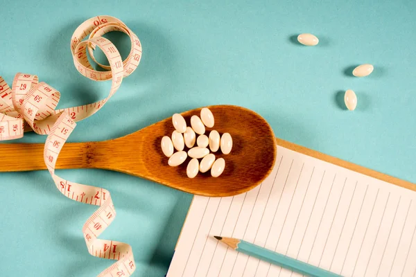 Sheet of Diet Plan and wooden spoon with a measuring tape on a blue background, diet, healthy lifestyle.