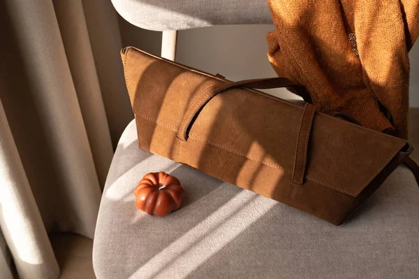 Moda sonbahar kıyafetleri ve aksesuar, karamel kahverengi çanta, güneş ışığı gölgeli sandalyede örgü, sonbahar mevsimlik kıyafet konsepti.