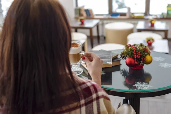 The girl drinks coffee in the winter in front of the window