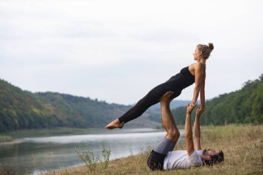 Erkek ve kız nehir kıyısında yoga yapıyorlar.