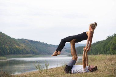 Erkek ve kız nehir kıyısında yoga yapıyorlar.
