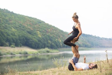 Erkek ve kız nehir kıyısında yoga yapıyorlar.