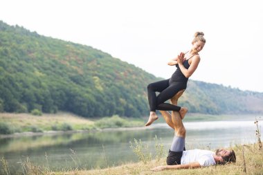 Erkek ve kız nehir kıyısında yoga yapıyorlar.