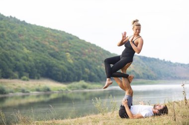 Erkek ve kız nehir kıyısında yoga yapıyorlar.