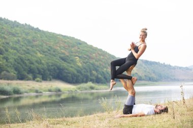 Erkek ve kız nehir kıyısında yoga yapıyorlar.