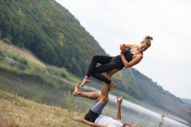 Erkek ve kız nehir kıyısında yoga yapıyorlar.