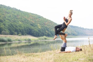 Erkek ve kız nehir kıyısında yoga yapıyorlar.