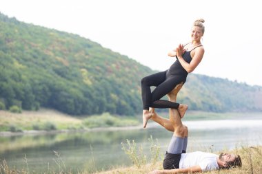 Erkek ve kız nehir kıyısında yoga yapıyorlar.