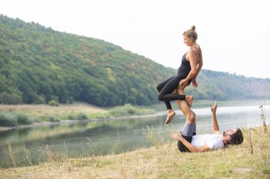 Erkek ve kız nehir kıyısında yoga yapıyorlar.
