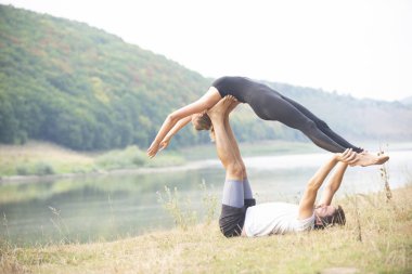 Erkek ve kız nehir kıyısında yoga yapıyorlar.