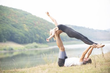 Erkek ve kız nehir kıyısında yoga yapıyorlar.