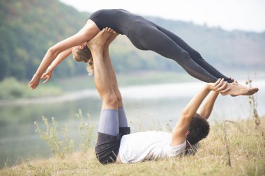 Erkek ve kız nehir kıyısında yoga yapıyorlar.