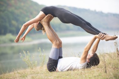 Erkek ve kız nehir kıyısında yoga yapıyorlar.