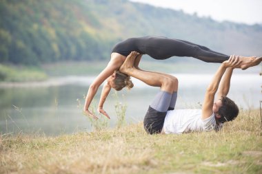 Erkek ve kız nehir kıyısında yoga yapıyorlar.