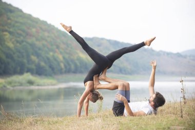 Erkek ve kız nehir kıyısında yoga yapıyorlar.