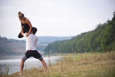 Erkek ve kız nehir kıyısında yoga yapıyorlar.