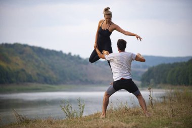 Erkek ve kız nehir kıyısında yoga yapıyorlar.