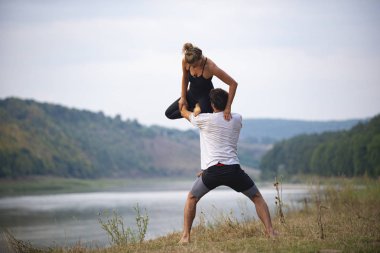 Erkek ve kız nehir kıyısında yoga yapıyorlar.