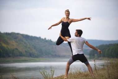 Erkek ve kız nehir kıyısında yoga yapıyorlar.