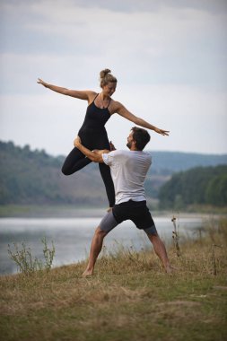 Erkek ve kız nehir kıyısında yoga yapıyorlar.
