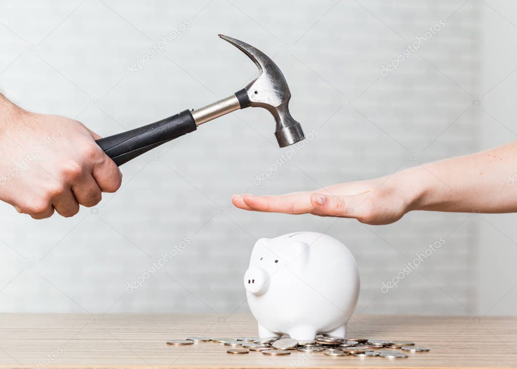 A hand holding a hammer which is raised above a white piggy bank