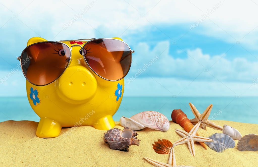 Summer piggy bank with sunglasses on beach