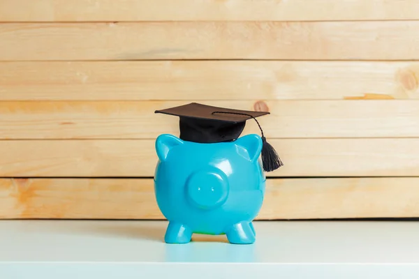 piggy bank with college graduate hat on wooden background