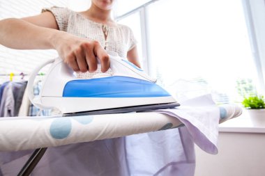 Ütü masasında giysileri ütüleyen bir kadın.